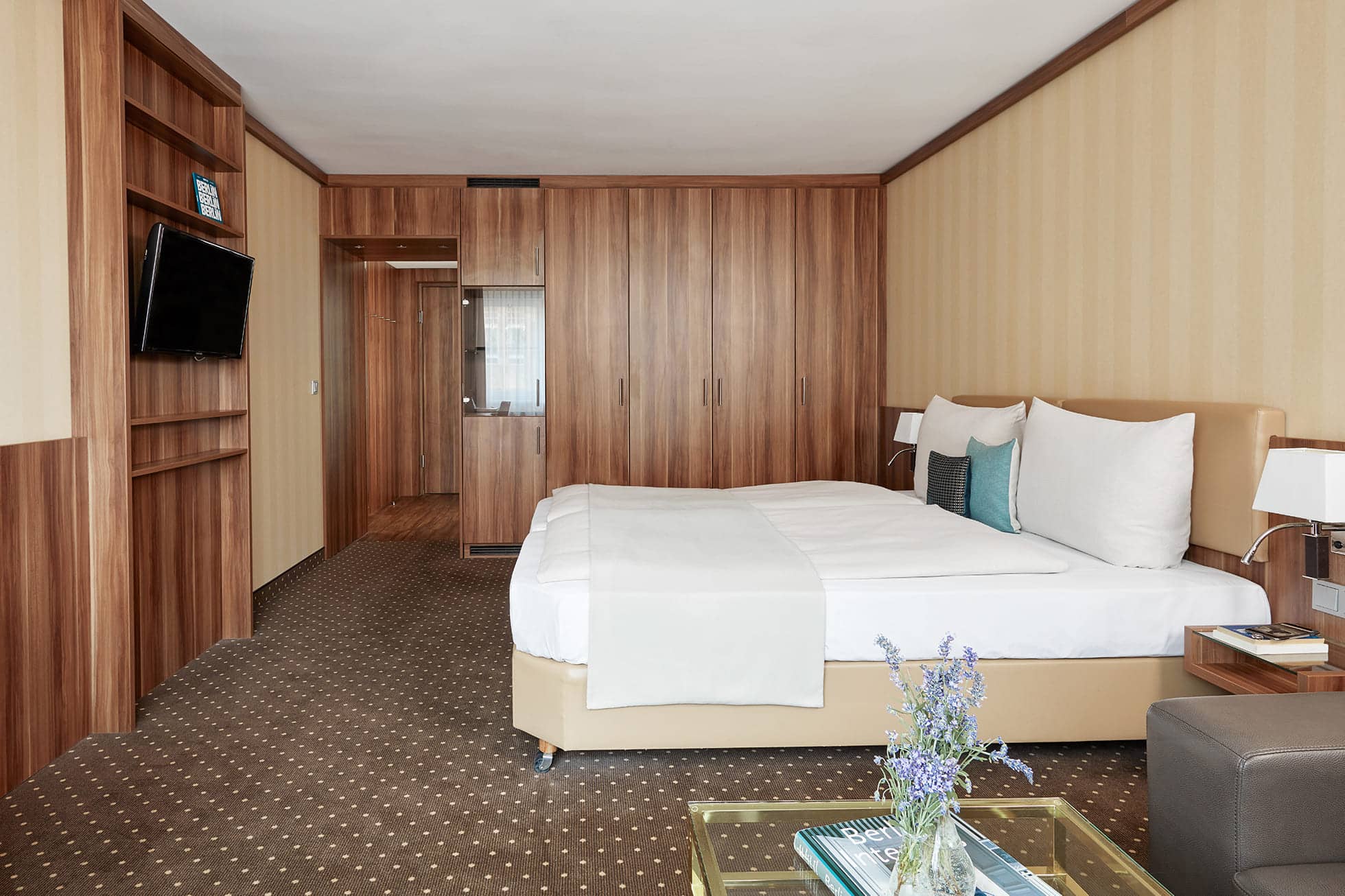 Living Hotel Berlin Mitte Deluxe Wohnbereich Foto mit Doppelbett, Fernseher, Sitzbereich und Zimmertür
