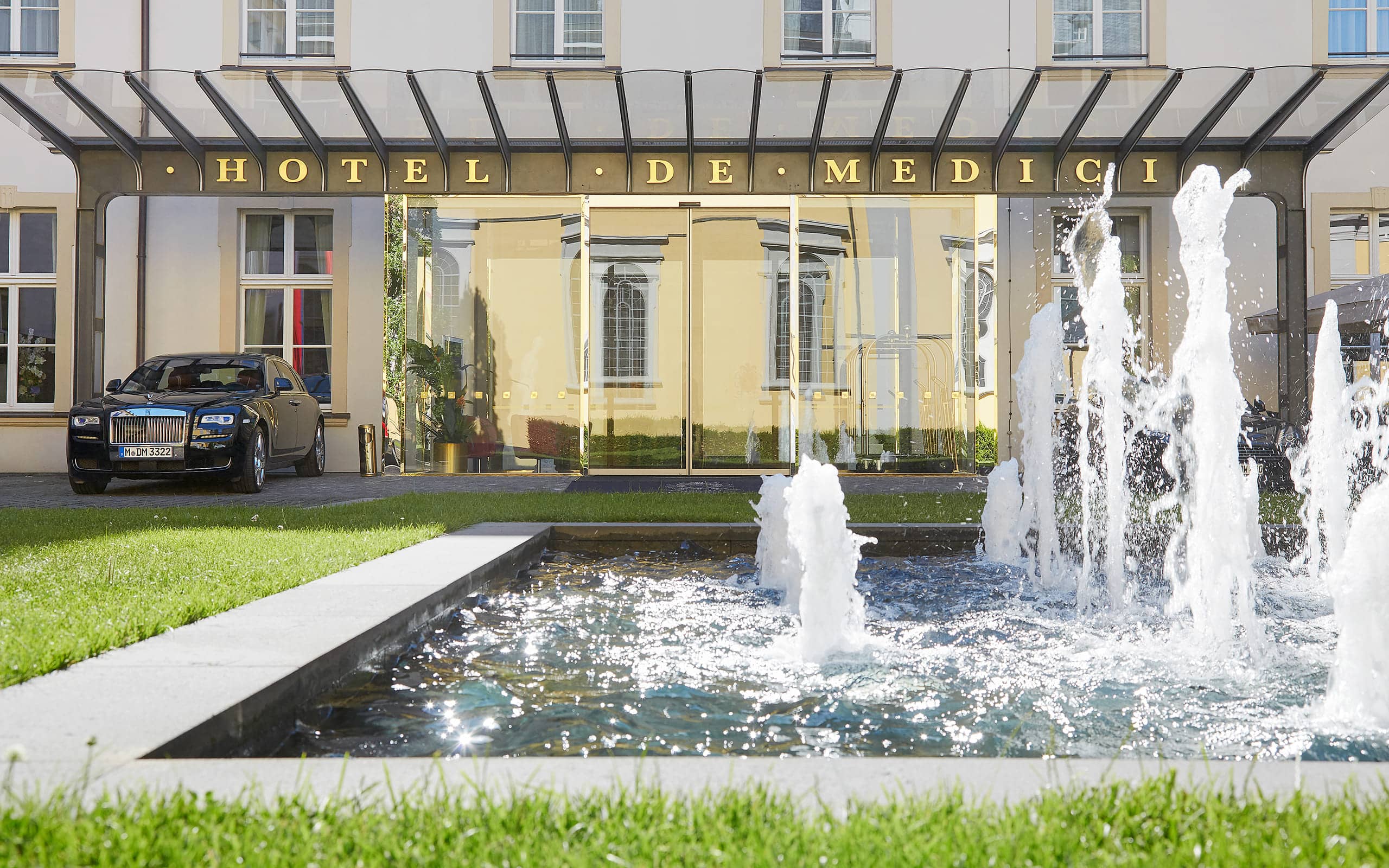 Fassade vom Living Hotel De Medici Frontansicht mir Auto und Springbrunnen