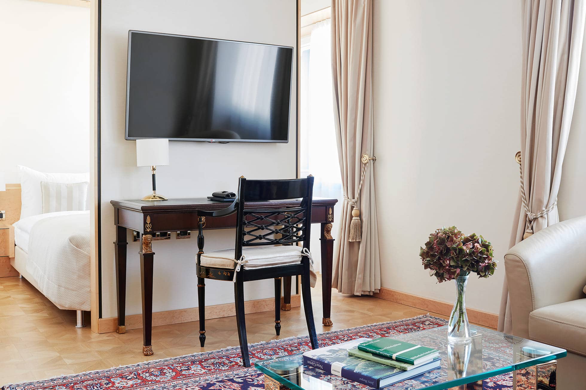 Gemütlich eingerichtetes Schlafzimmer mit Schreibtisch, gemütlicher Sitzecke und Fernseher