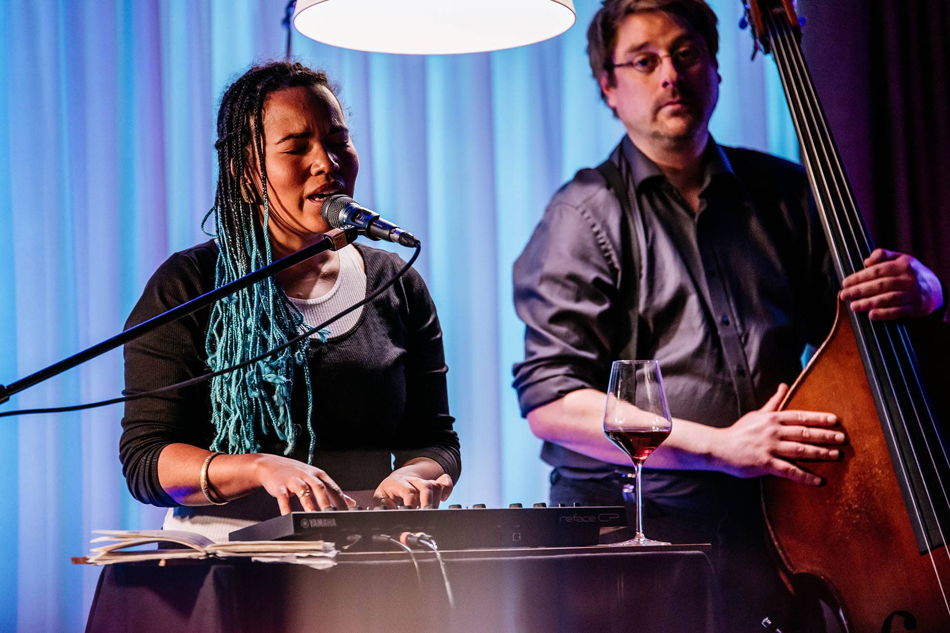 Sängerin am Klavier mit blauen Dreadlocks und ein Mann am Kontrabass zu ihrer Seite