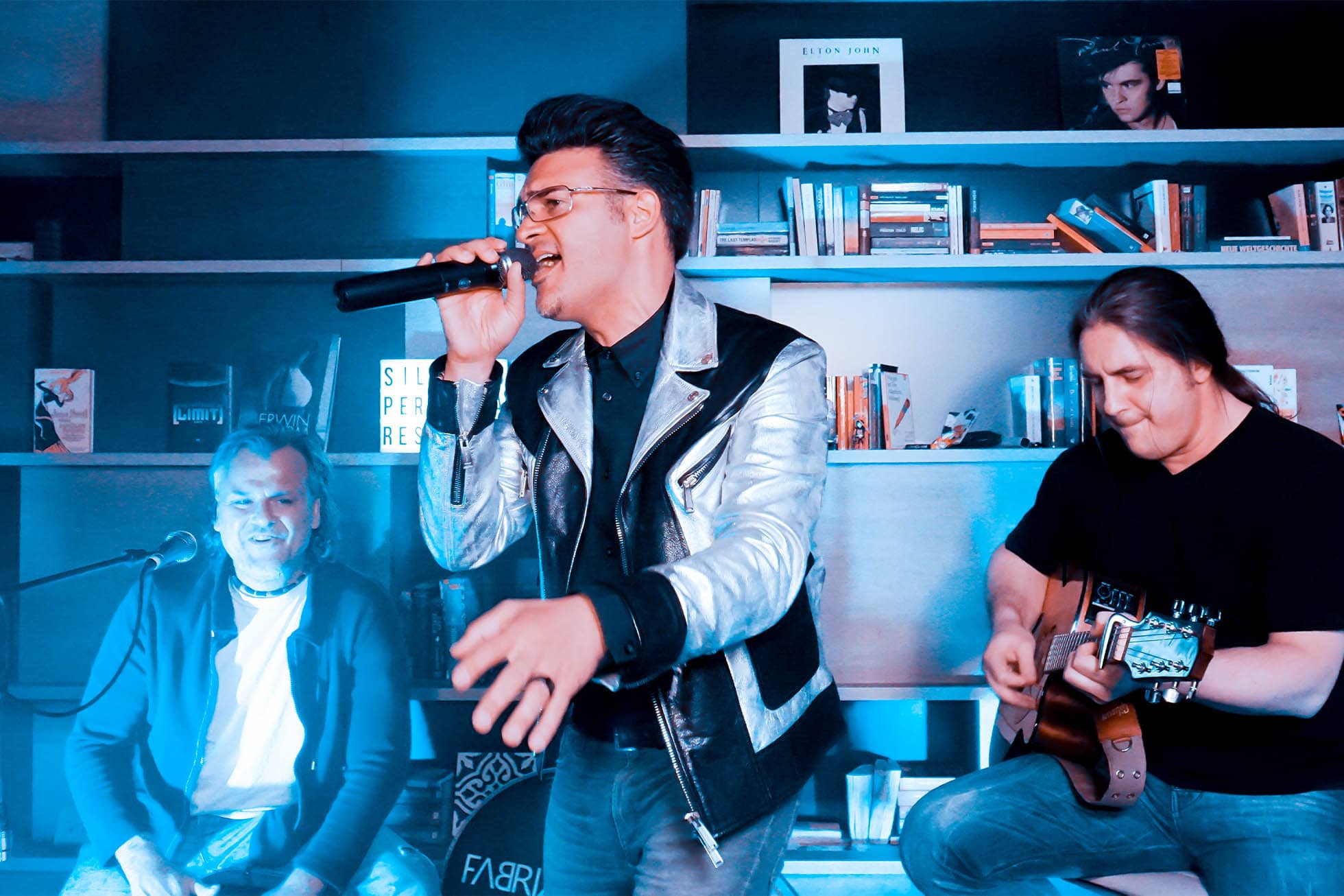 Sänger mit Mikrofon am Singen im Living Room mit Gitarristen im Hintergrund