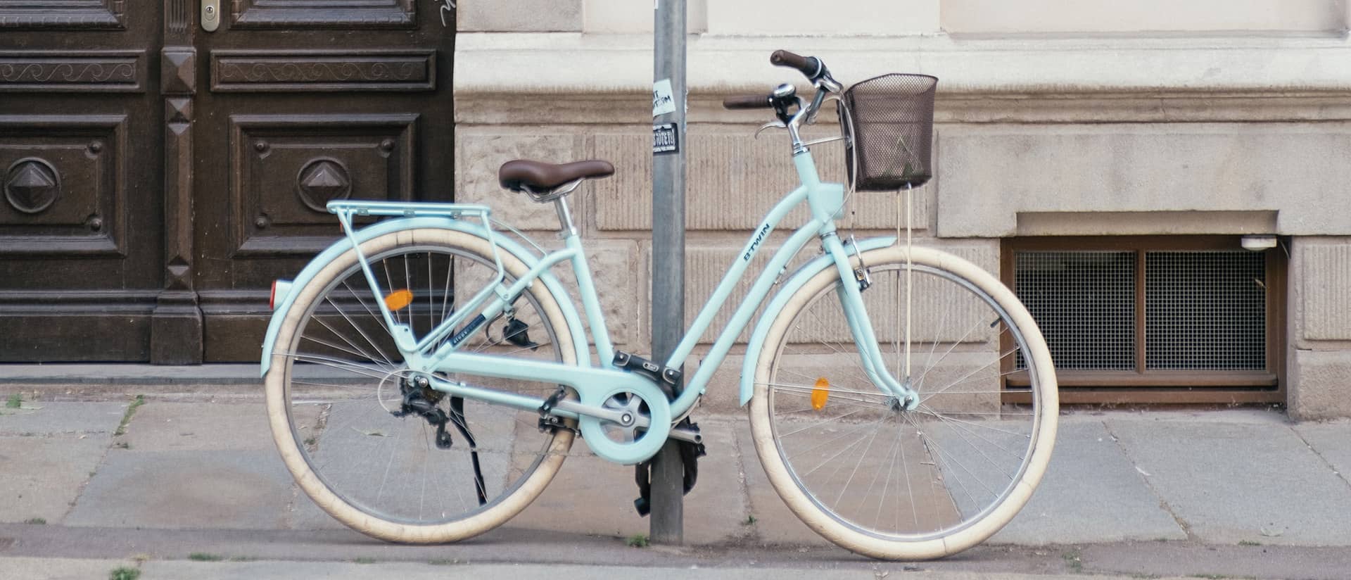 Hellblaues City-Fahrrad mit Korb, an einen Laternenpfahl vor einer Hausfassade angelehnt.