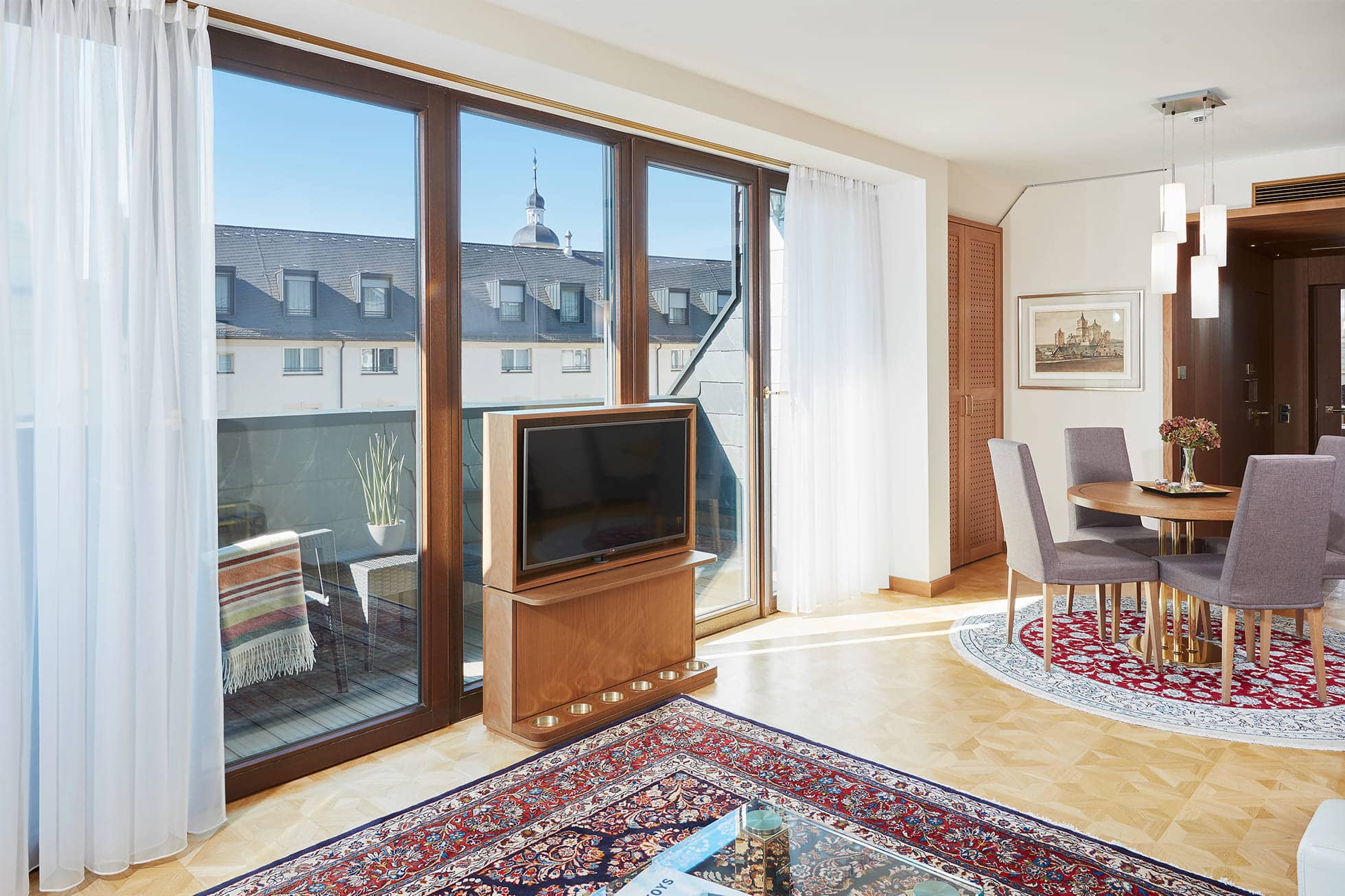Serviced Apartment mit Fernseher vor Fenster, rundem Esstisch mit Stühlen und Teppichboden.